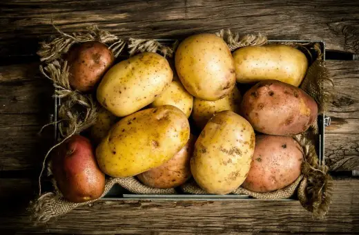 Ziemniaki w metalowej skrzynce, wyłożonej jutą, na drewnianym tle. Wyglądają jak zdrowe nerki, gotowe do przygotowania pysznego posiłku.