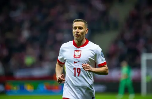 Frankowski piłkarz w białej koszulce z orłem na piersi, numer 19. Biegnie po boisku, skupiony na grze.