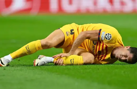 Piłkarz w żółtej koszulce leży na trawie, trzymając się za nogę. Wygląda na to, że Robert Lewandowski kontuzja uniemożliwiła mu dalszą grę.