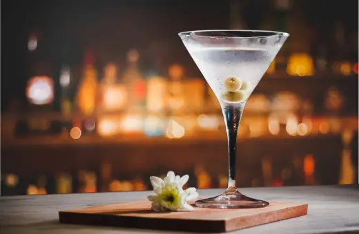 Kryształowy kieliszek z martini, trzema oliwkami i białą kwiatową ozdobą. Idealny drink, z czym pić martini?