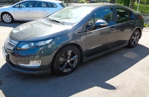 Ciemnoszary Chevrolet Volt stoi na parkingu. Obok niego widać srebrne kombi.