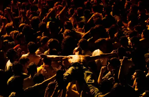 Tłum szaleje w moshpit, unosząc nagiego mężczyznę z rozłożonymi ramionami.