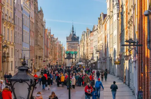 Tłum ludzi spaceruje ulicą Długą na gdańskiej starówce, podziwiając kolorowe kamienice i zabytkową architekturę.
