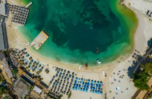 Widok z lotu ptaka na turkusowe morze i piaszczyste **albania plaże** z leżakami, parasolami i ludźmi cieszącymi się słońcem.