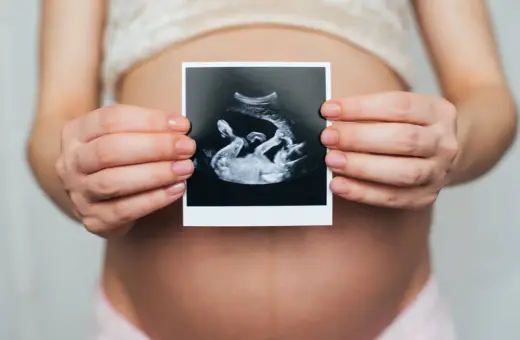 Ciężarna kobieta trzyma zdjęcie USG, na którym widać dziecko. Widać też łożysko na przedniej ścianie.
