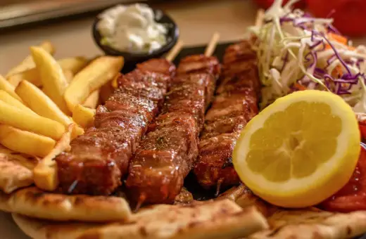Pyszne souvlaki na patyczkach, podane z frytkami, pitą, surówką i cytryną.