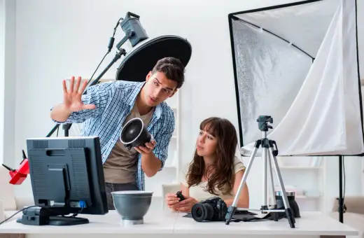 Mężczyzna, technik fotografii i multimediów, pokazuje kobiecie lampę. W tle sprzęt studyjny.