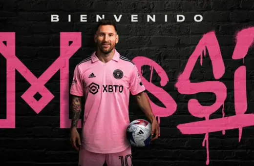 Lionel Messi w różowej koszulce Inter Miami, z piłką w ręku, na tle napisu "Bienvenido Messi". Nowy inter miami trener.