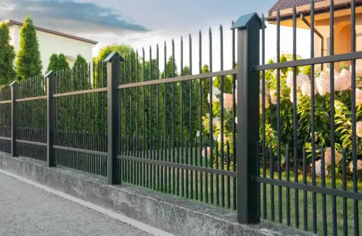 Betonowy murek jako alternatywa dla podmurówki pod ogrodzenie. Czarny metalowy płot z ostrymi zakończeniami.