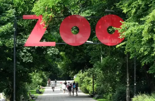 Duże czerwone litery "ZOO" nad alejką w zielonym parku. Ludzie spacerują, ciesząc się dniem w zoo w Polsce.