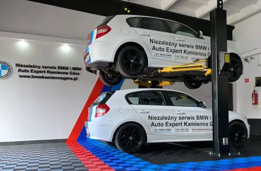 Dwa białe BMW, jedno na podnośniku, w serwisie Auto Expert. W tle logo BMW.