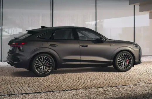 Elegancki Audi Q3 2025 w ciemnym kolorze, z dynamiczną linią nadwozia, prezentuje się na tle nowoczesnej architektury.