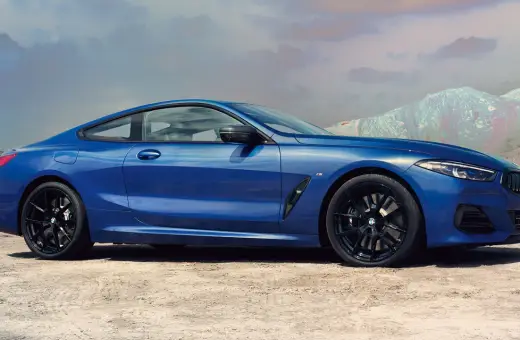 Błękitne BMW 840i z czarnymi felgami na tle pustynnego krajobrazu i gór.