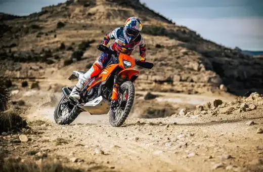 Motocyklista w kasku i stroju crossowym śmiga pomarańczowym motocyklem po pustynnym terenie. Czy na crossa trzeba mieć prawo jazdy?