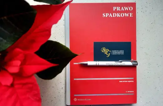 Czerwona książka "Prawo spadkowe" obok poinsecji. Długopis z nazwiskiem adwokatki i wizytówka kancelarii sugerują tematykę prawną, być może związaną z zapisem windykacyjnym.