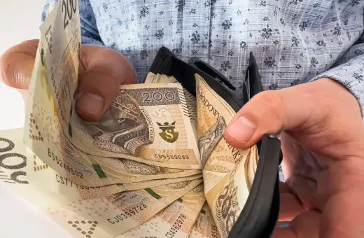 Ręce trzymają portfel z banknotami 200 zł. Ile trzeba przepracować, by tyle zarobić?
