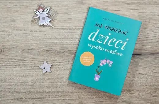 Książka "Jak wspierać dzieci wysoko wrażliwe" na drewnianym tle, obok aniołka i gwiazdki.