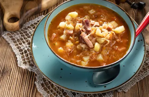 Aromaticzny kapuśniak jak u babci, pełen ziemniaków i wędzonki, w niebieskiej misce na drewnianym stole.