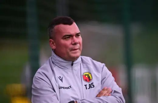 Trener Jagiellonii, z rękami skrzyżowanymi na piersi, w szarej kurtce z herbem klubu.