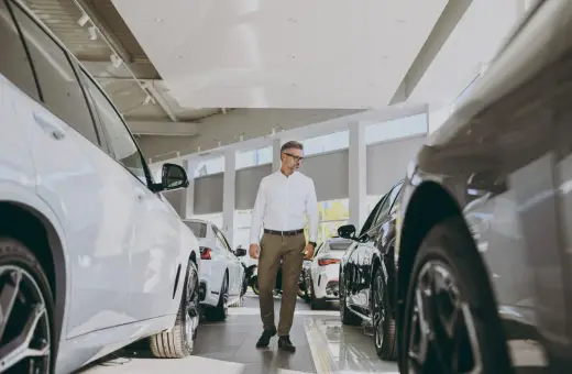 Elegancki mężczyzna w okularach wybiera nowe auto do miasta w salonie samochodowym. Wokół lśniące pojazdy.