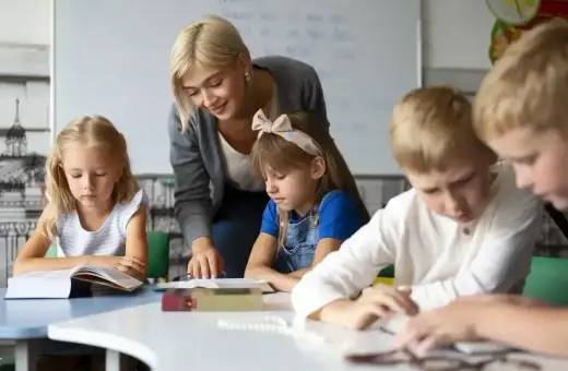 Nauczycielka wspiera uczniów w nauce, pokazując swoje kompetencje rady pedagogicznej. Dzieci skupione na książkach.
