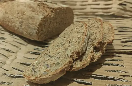 Chleb orkiszowy, pokrojony na kromki, z widocznymi ziarnami, leży na falistej tekturze.