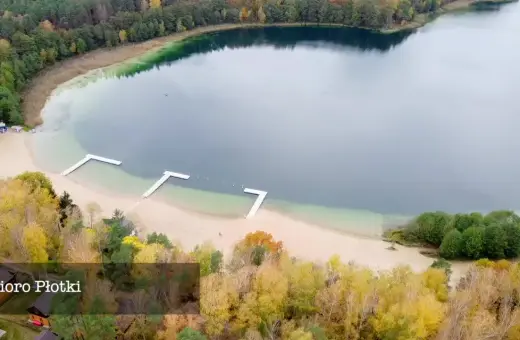 Jesioro Płotki jesienią. Piękna plaża, drewniane pomosty i kolorowe drzewa otaczają spokojną taflę wody.