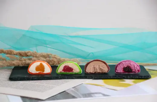 Cztery kolorowe mochi: pomarańczowe, zielone z malinami, czekoladowe i fioletowe z jagodami. Różne rodzaje słodkości.