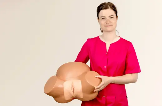 Kobieta w różowej bluzce prezentuje model miednicy do nauki masażu krocza przed porodem.