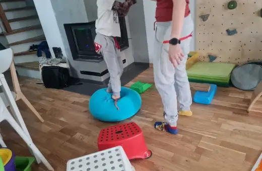 Dziecko ćwiczy równowagę na niebieskiej poduszce, część domowej ścieżki sensorycznej dla dzieci.