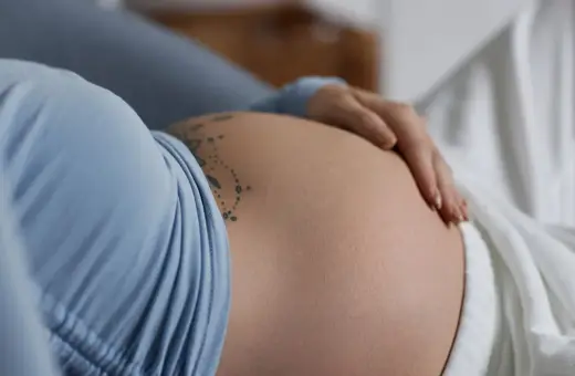 Dłoń delikatnie głaszcze ciążowy, twardy brzuch z tatuażem.