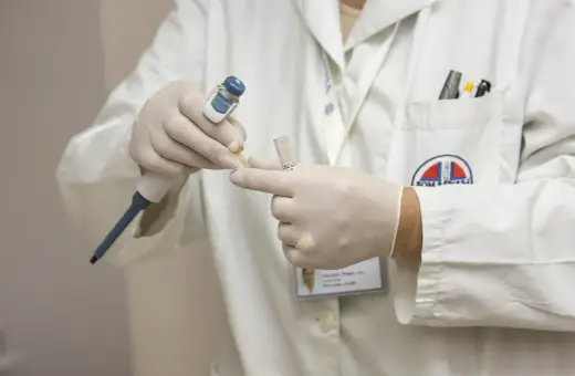 Laborant w białym fartuchu, rękawiczkach i z identyfikatorem przygotowuje próbkę do analizy. To kluczowy etap przed obdukcją.
