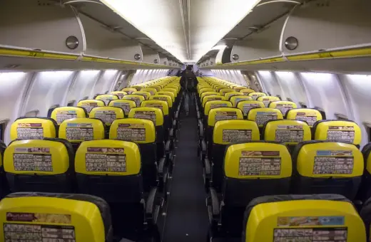 Puste rzędy żółtych siedzeń w samolocie Ryanair. Widać instrukcje bezpieczeństwa na oparciach.
