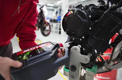 Osoba w czerwonej bluzie wlewa olej Motul do silnika motocykla crossowego 4T.