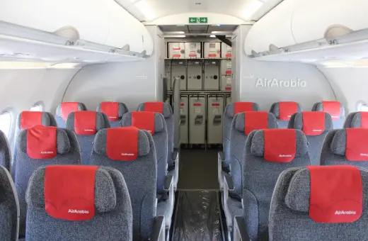 Wnętrze samolotu Air Arabia z rzędami szarych siedzeń i czerwonymi zagłówkami. W tle widać wózki pokładowe. Dobre **air arabia opinie** potwierdzają komfort podróży.