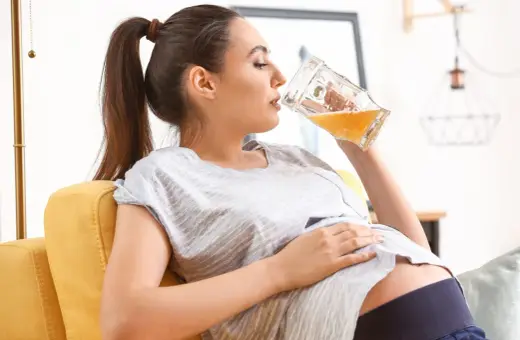 Kobieta w ciąży pije piwo bezalkoholowe z dużego kufla, relaksując się na kanapie.