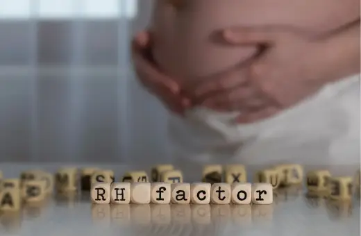 Ciąża i czynnik Rh. W tle brzuch kobiety, na pierwszym planie kostki z napisem "RH factor". Immunoglobulina w ciąży może być kluczowa.