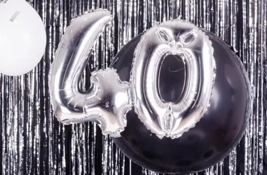 Srebrne balony z cyfrą 40 i biały balon na tle błyszczącej kurtyny. Idealne na zabawy na 40 urodziny!