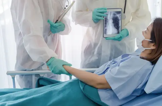 Lekarze w kombinezonach ochronnych wspierają pacjentkę w szpitalu, pokazując jej zdjęcie płuc na tablecie. Nadzieja na powrót do zdrowia dzięki leczeniu, być może z użyciem remdesivir.