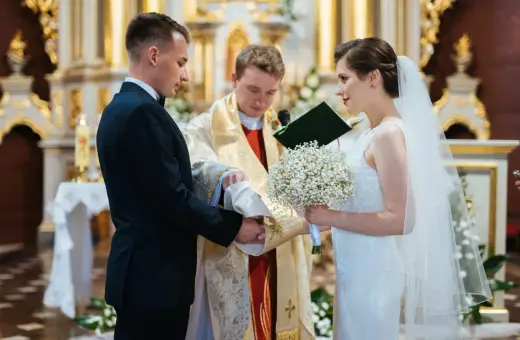 Panna młoda w welonie i z bukietem, pan młody w garniturze, podczas ceremonii ślubnej w kościele.