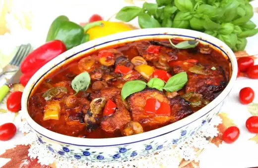 Schab po cygańsku z pieczarkami i papryką w sosie pomidorowym, udekorowany bazylią. Danie wygląda apetycznie.