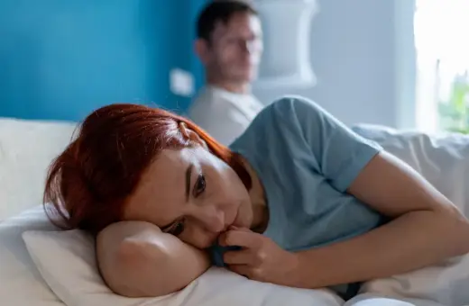 Smutna kobieta leży w łóżku, zamyślona. W tle niewyraźny mężczyzna. Obraz symbolizuje trudne relacje i toksyczny partner cechy.