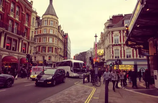 Tętniące życiem ulice Soho w Londynie, z charakterystyczną architekturą, autobusami i ludźmi spacerującymi po chodniku.