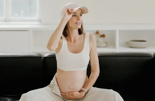 Kobieta w ciąży, czując uderzenia gorąca, poprawia czapkę. Siedzi na czarnej kanapie w jasnym wnętrzu.