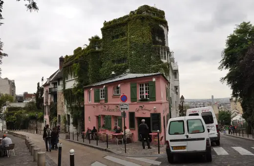 Urokliwa ulica na Montmartre z różową kawiarnią La Maison Rose i budynkiem porośniętym bluszczem.