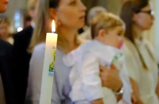 Chrzest dziecka. Czy świadek chrztu musi mieć zaświadczenie? Płonąca świeca chrzcielna w dłoniach.