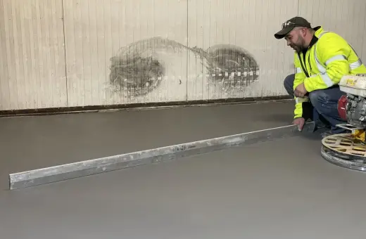 Pracownik w kamizelce odblaskowej wykonuje poziomowanie wylewki betonowej za pomocą łaty.