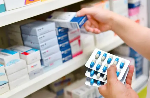 Ręka farmaceuty wybiera z półki lek, w tym antybiotyk azytromycyna w blistrach.