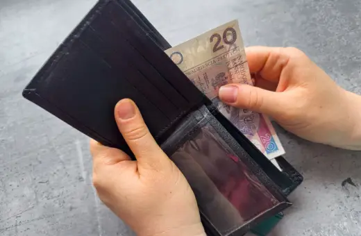 Ręce wkładają banknot 20 zł do portfela. Zastanawiasz się, po jakim czasie od zarejestrowania wypłacany jest zasiłek dla bezrobotnych?