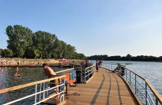 Ludzie odpoczywają i kąpią się nad zalewem Borki. Drewniane molo zaprasza do spacerów i podziwiania widoków.